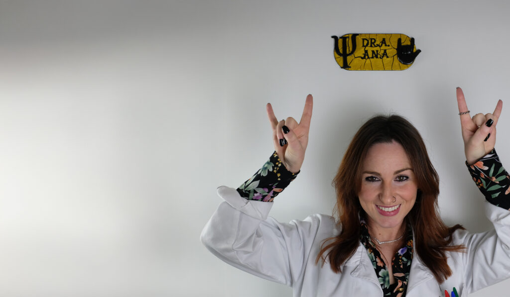 Ana Félix a sorrir e a fazer o sinal de rock com a mão, junto à placa do seu consultório