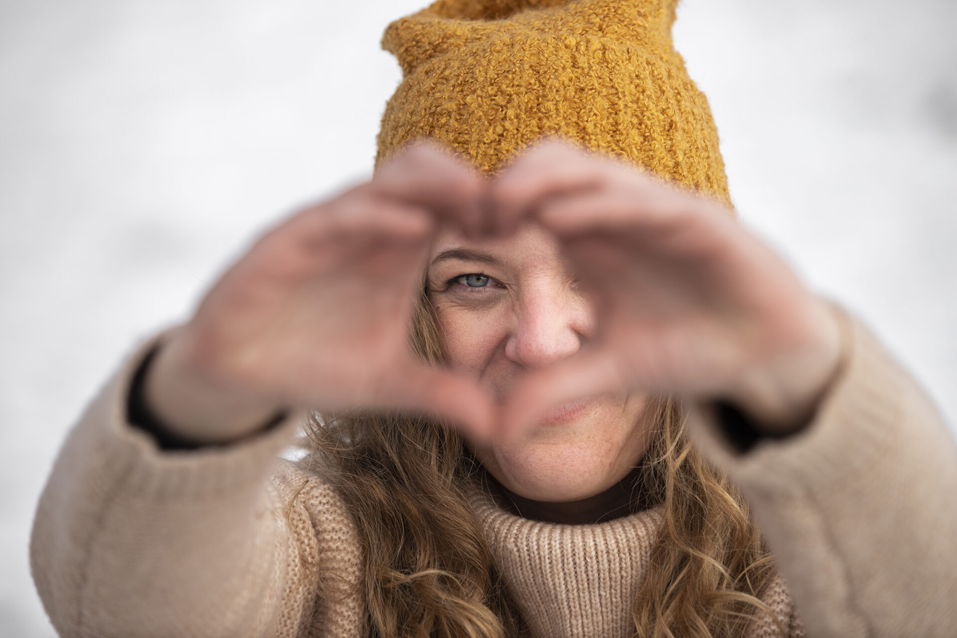 Mulher de gorro amarelo faz um coração com as mãos à frente do rosto