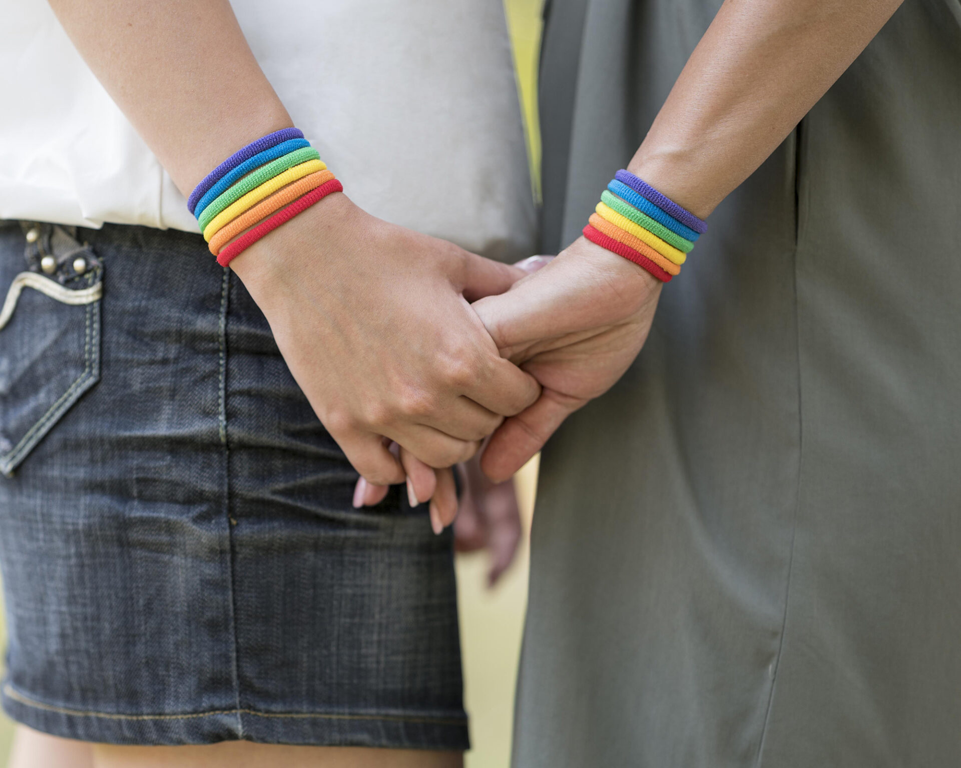 Duas pessoas de mãos dadas, com pulseiras de arco-íris nos pulsos