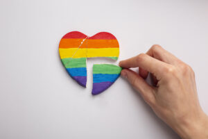 Coração com as cores do arco-íris partido ao meio, com uma mão a segurar uma das metades