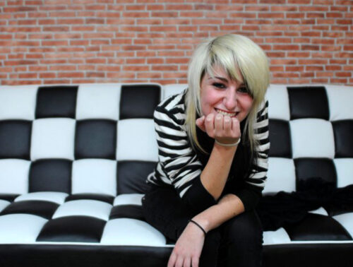 Ana Félix jovem, de cabelo loiro, a rir num sofá aos quadrados pretos e brancos